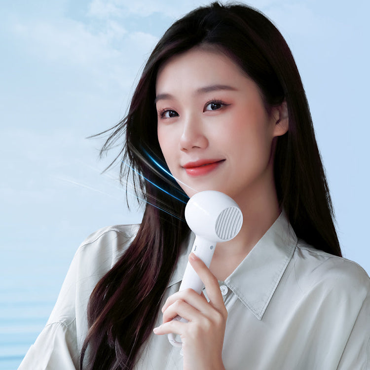Woman cooling off with a Magnussen handheld Airflow fan by the sea